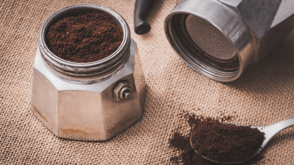 Ein Espressokocher liegt auseinander gebaut auf dem Tisch, im Filtereinsatz ist frisch gemahlener Kaffee.