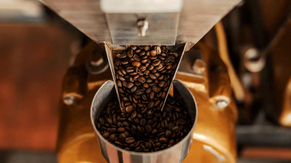 Kaffeebohnen fließen in den Behälter einer Kaffeemühle, wo sie gemahlen werden.
